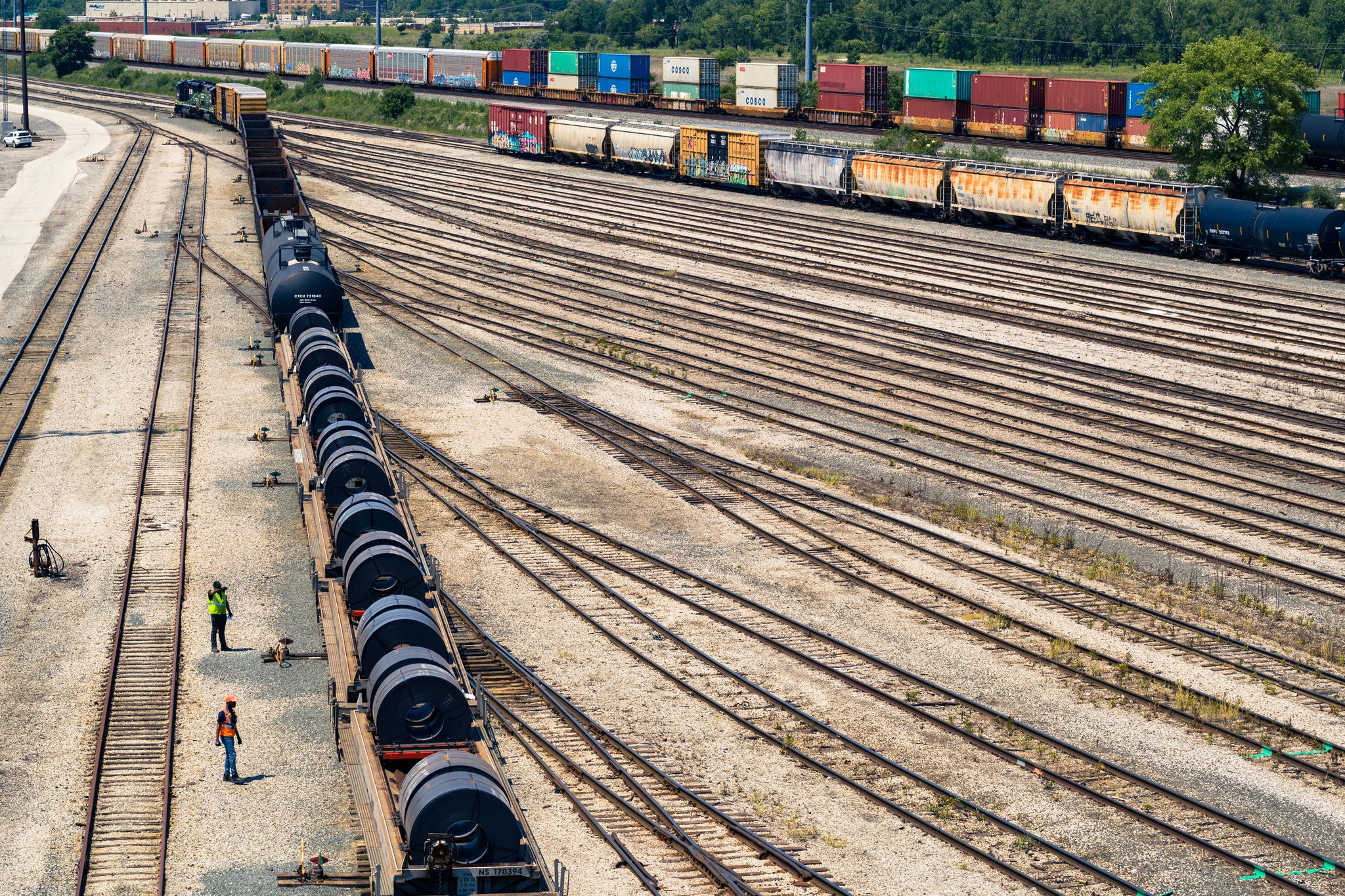 Aerial view of a train leaving a yard with other trains behind that are shipping metals by rail