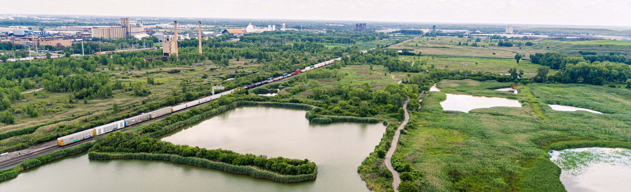 Aerial of water next to a train track with a city in the background, prime industrial development spot