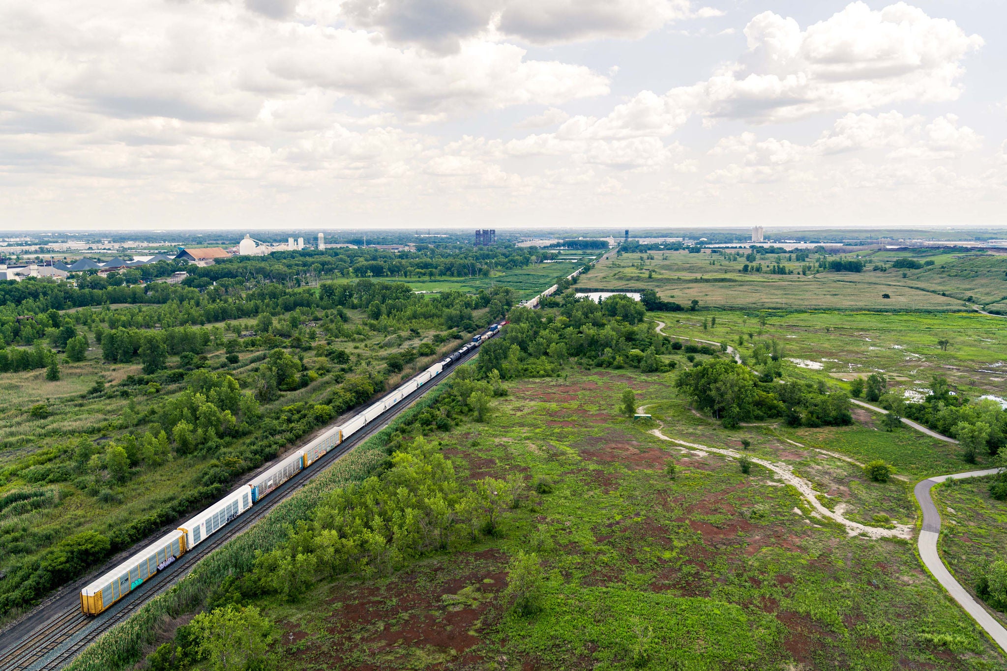 Wide aerial view of a train passing through an industrial development site being built in a field